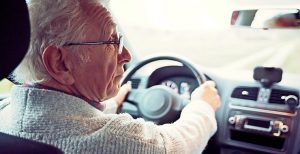An elderly man looks to the side as he drives