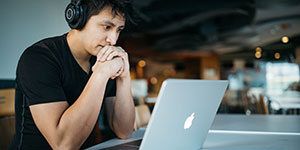 A student looks at their laptop while wearing a pair of headphones